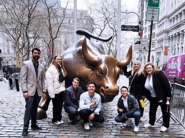 Students pose with a bull statue on wall street.